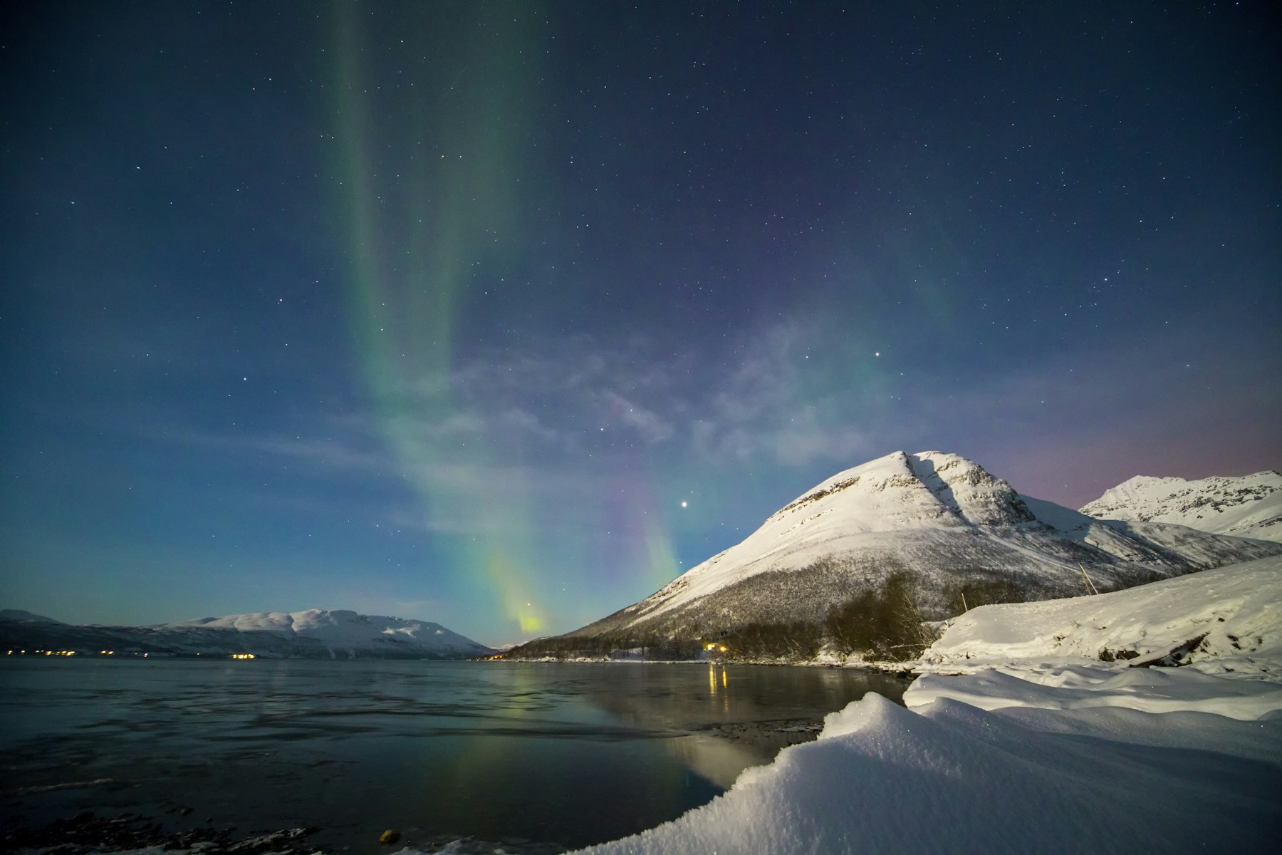 Northern lights above snow-covered mountains and a fjord near Tromsø, Norway